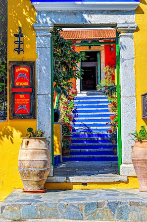 A colorful entrance with a sign for 'Garden Studios' and a telephone number, leading to a staircase with blue steps and potted plants. - Symi Garden Studios (Symi)