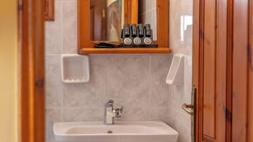Un baño con un lavamanos pedestal, un espejo con marco de madera y un estante pequeño con artículos de aseo.