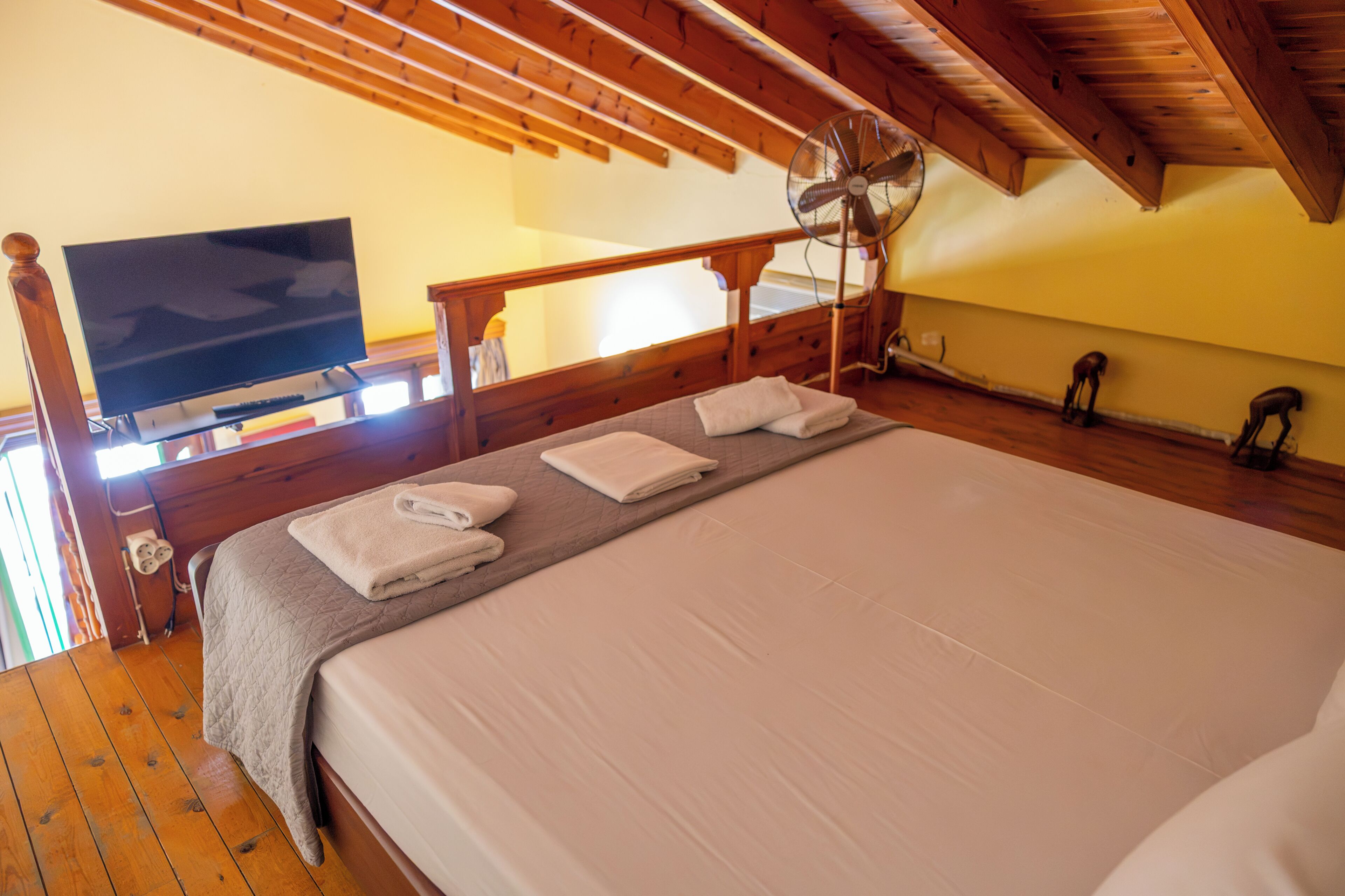 Un dormitorio con cama, televisor, ventilador y vigas de madera.