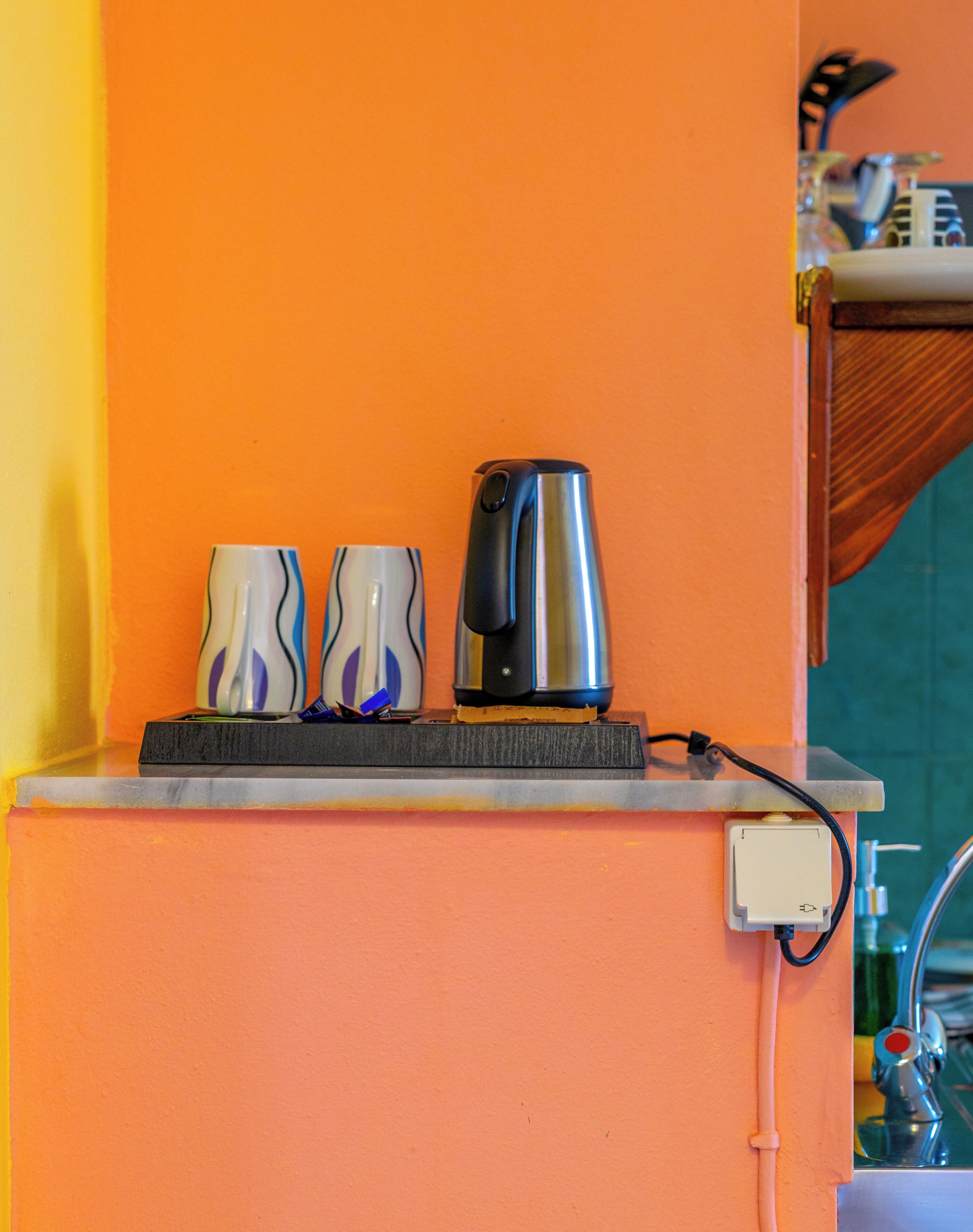 A kitchen counter with a kettle, two mugs, and a power outlet.