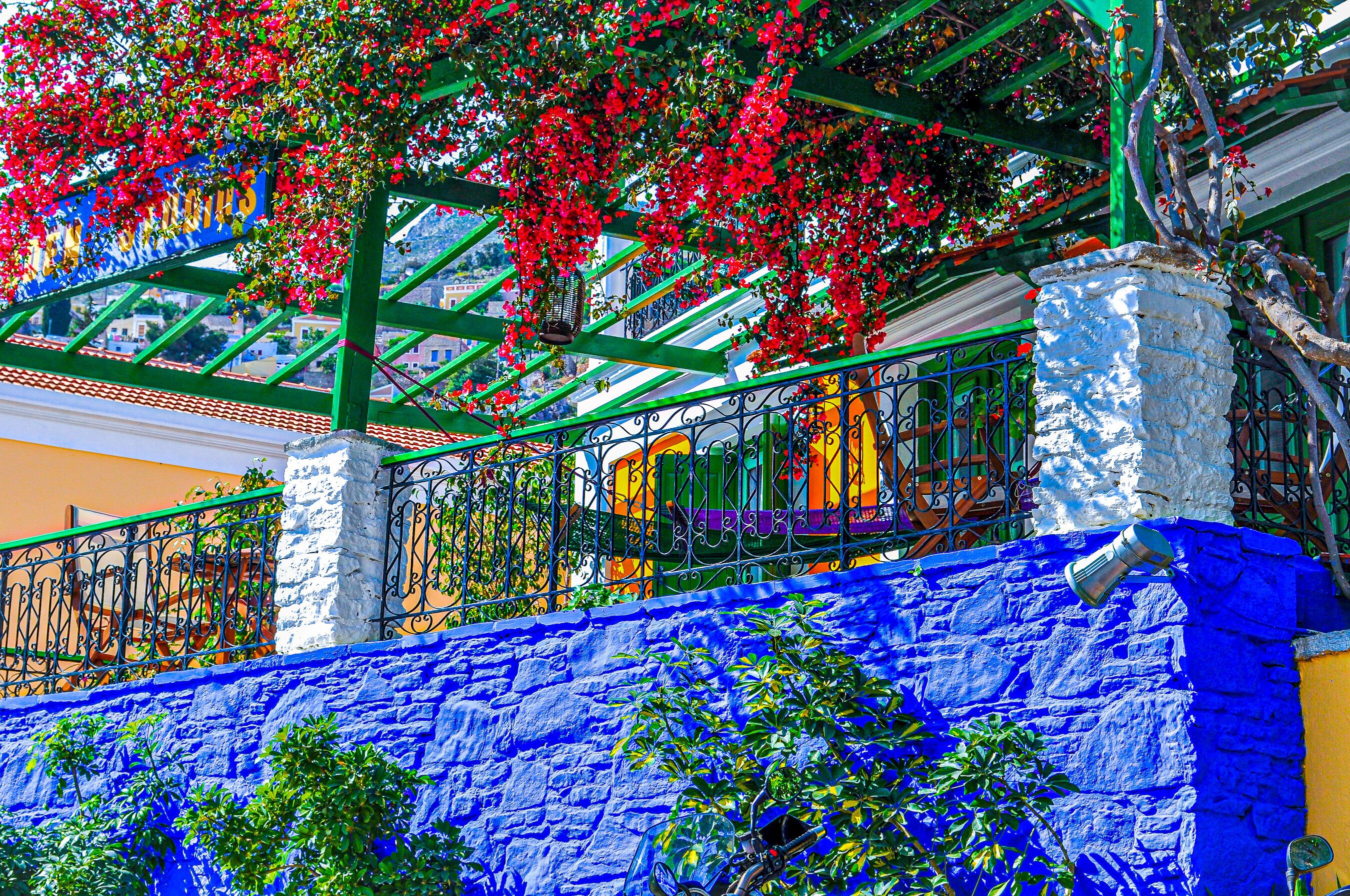 Un balcon animé, agrémenté de fleurs rouges, avec un mur bleu et une rambarde en métal.