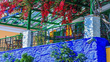 Un balcon animé, agrémenté de fleurs rouges, avec un mur bleu et une rambarde en métal.