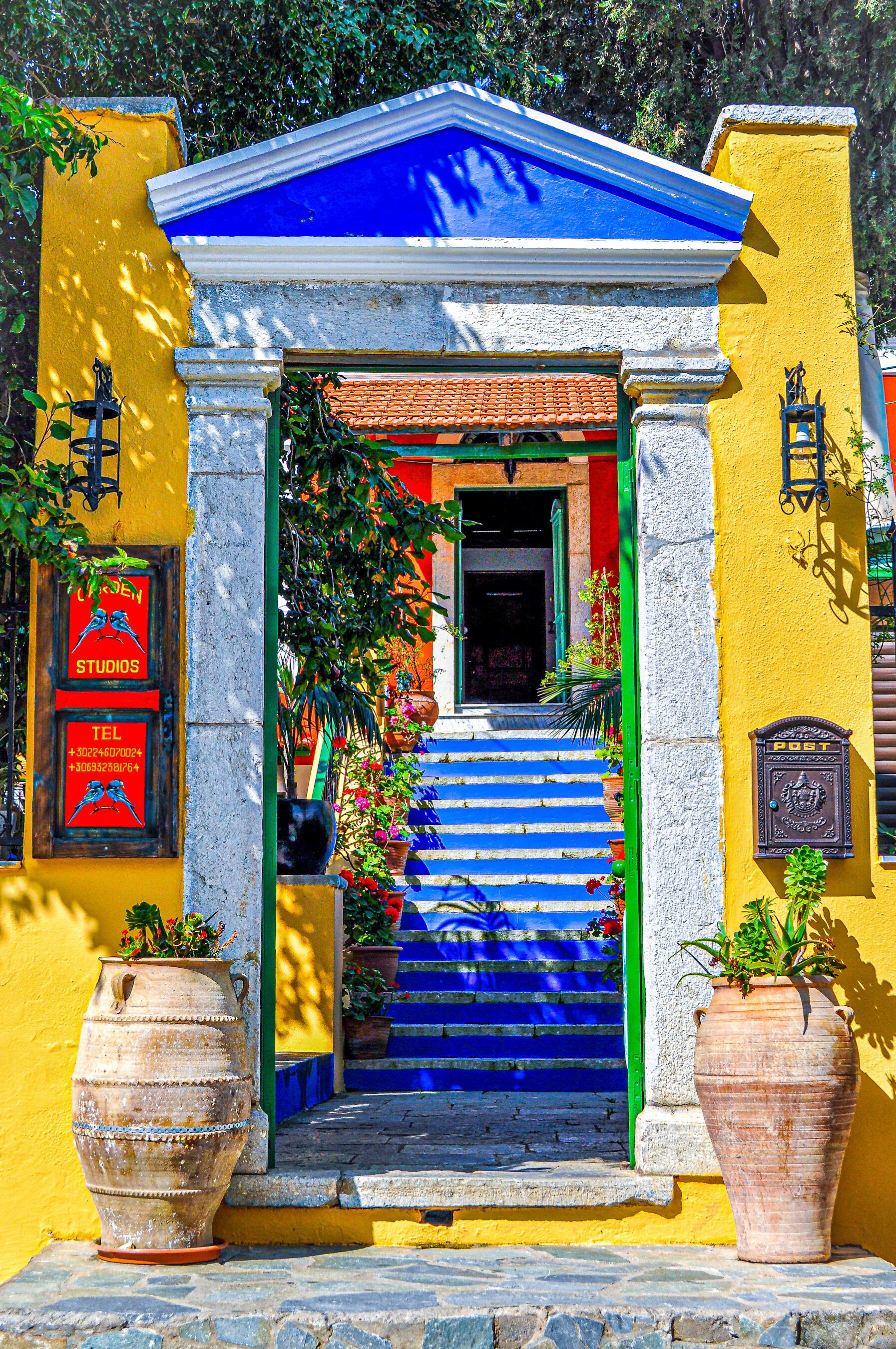 Un edificio colorido con techo azul, un conjunto de escaleras que conducen a una puerta y dos macetas grandes en el suelo.