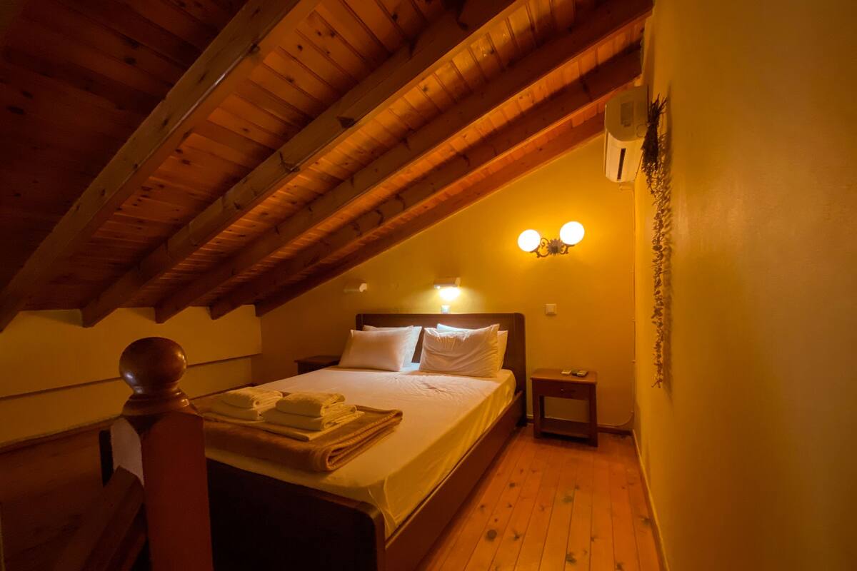 Ein Schlafzimmer mit Holzbalkendecke, einem Bett mit weißen Leinen, zwei Nachttischlampen und einem Nachttisch mit Telefon.