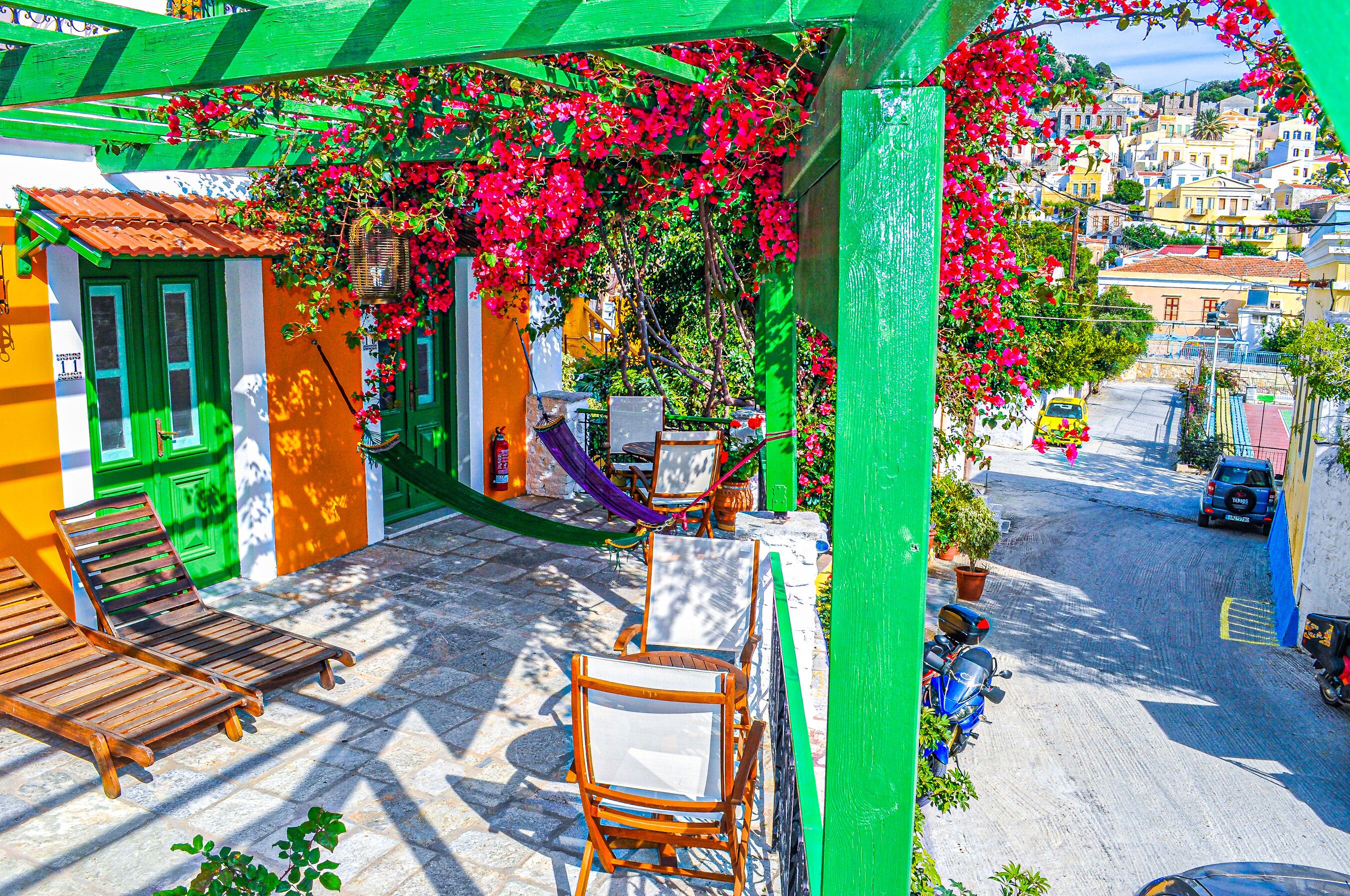 Una terraza con sillas y mesa de madera, un toldo verde y flores rojas.