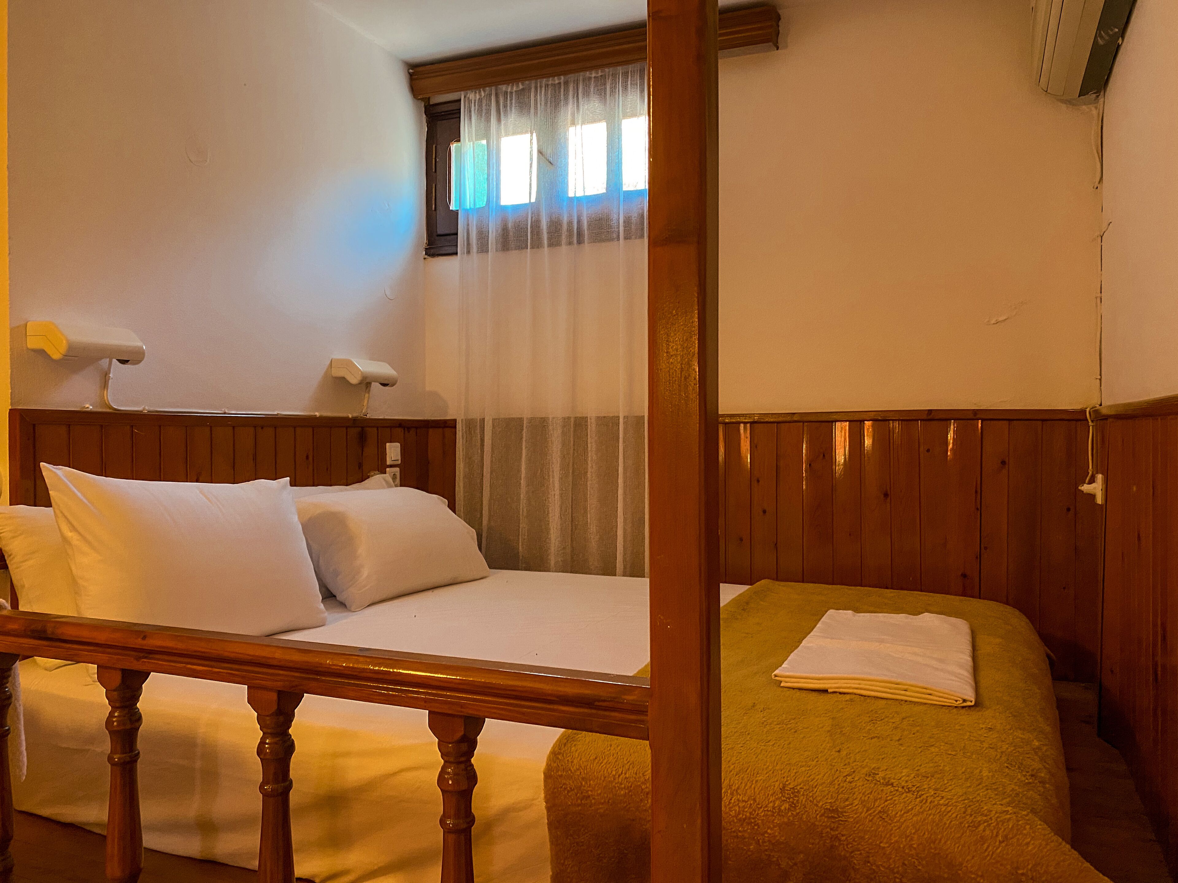 Una habitación con cama de madera, cabecera de madera, ventana con cortinas y una lámpara de noche.