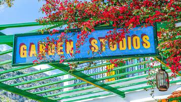 Et skilt for 'Garten Studios' med en grøn metalramme og blå baggrund, omgivet af røde blomster.