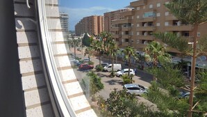Un edificio de varios pisos con balcones, un estacionamiento con coches y palmeras.