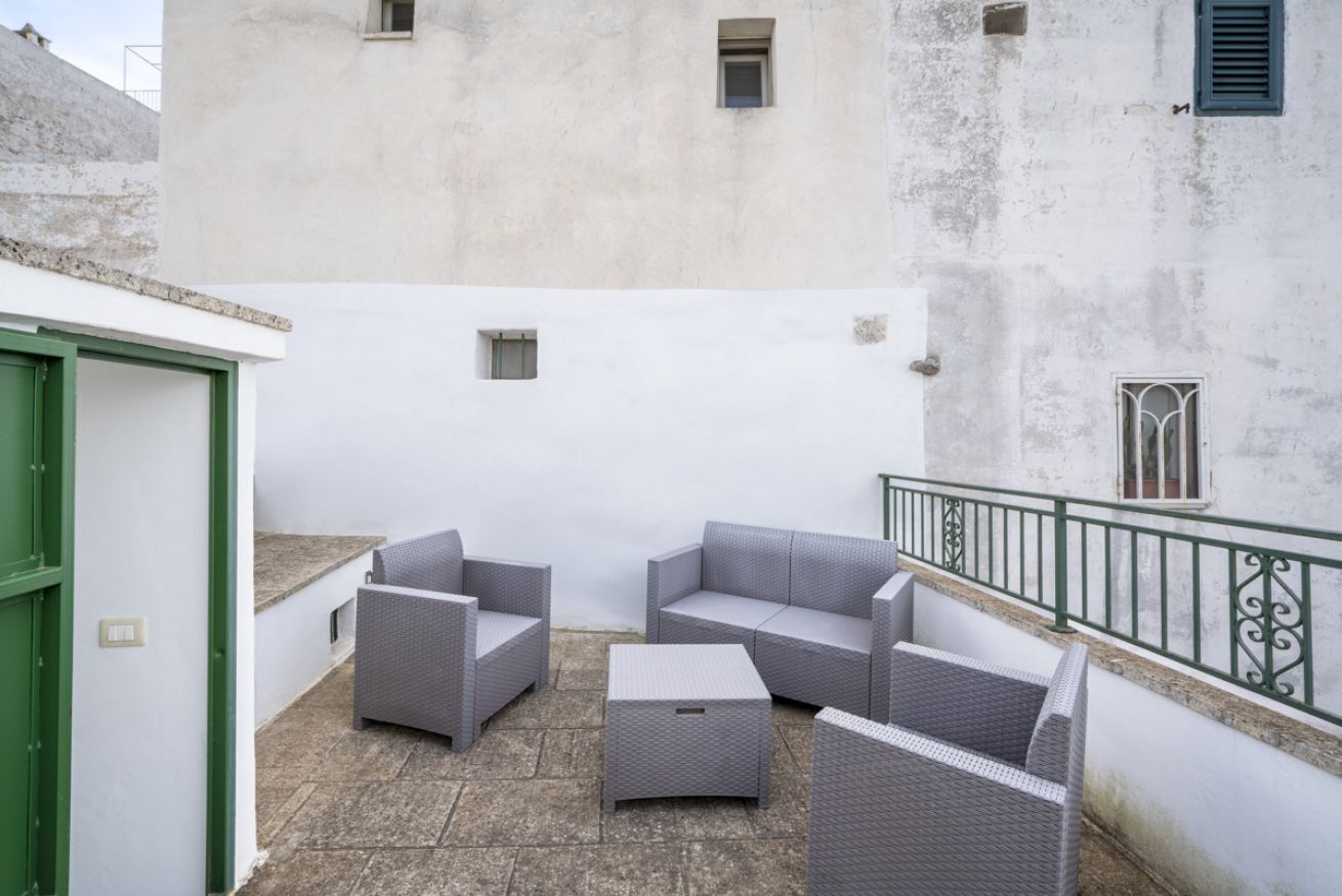 A courtyard with outdoor furniture, a white building, and a green railing.