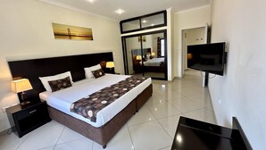 A modern hotel room with a large bed, bedside lamps, a flat-screen TV, and a large mirror. - Hotel Fátima  (Tete)