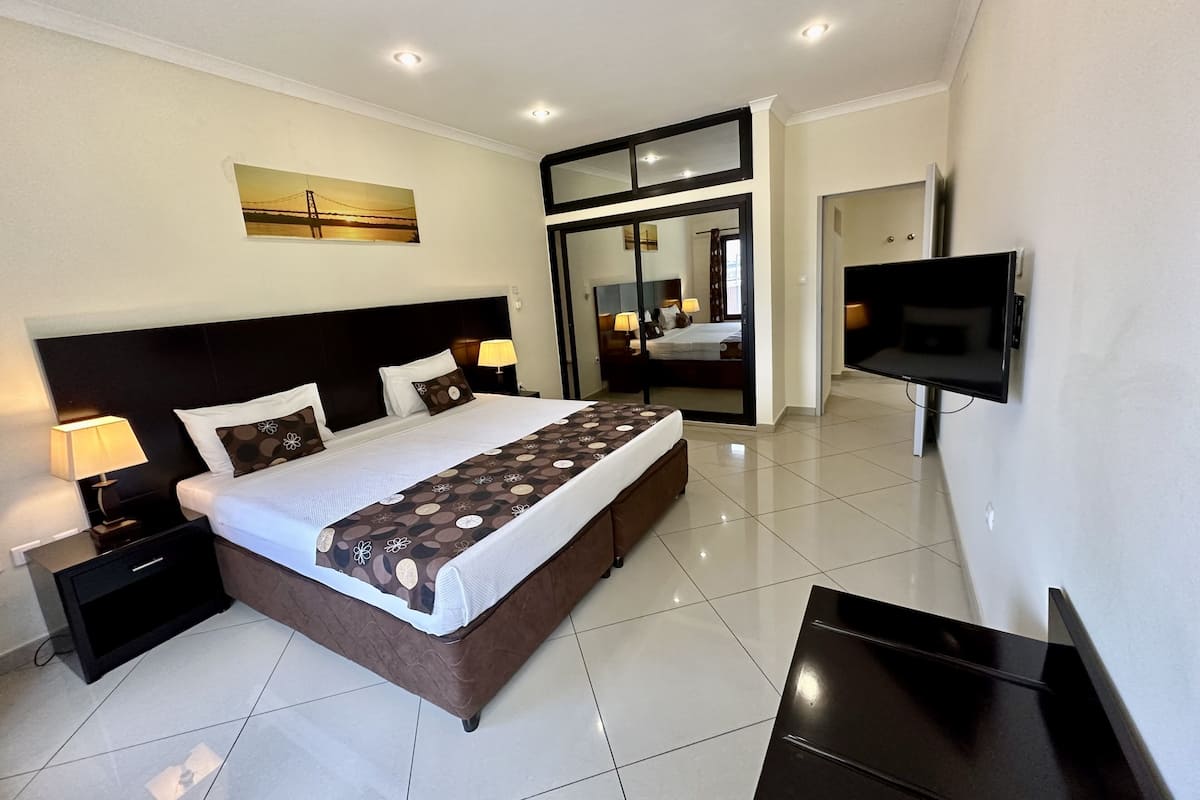 A modern hotel room with a large bed, bedside lamps, a flat-screen TV, and a large mirror.