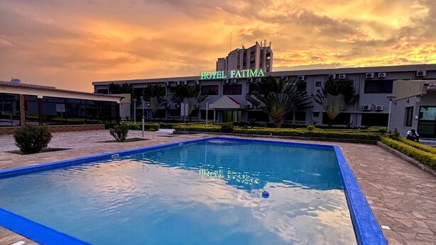 A swimming pool with a blue edge, surrounded by stone tiles, and a hotel building in the background. - Hotel Fátima  (Tete)