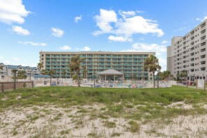 A beachfront hotel with multiple balconies, a pool area, and palm trees. - Plantation Dunes Condos (Gulf Shores)