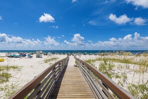 A wooden boardwalk leading to a beach with umbrellas and beach chairs. - Plantation Dunes Condos (Gulf Shores)