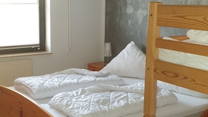 A single wooden bed with white bedding in a room with a large window and a gray wall.