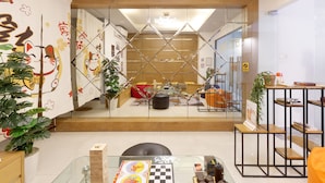 A modern hotel lobby with a glass partition, wooden flooring, and a variety of seating areas including a bench and a table with a chessboard. - Saigon Authentic Hostel & Tours (Ho Chi Minh City)