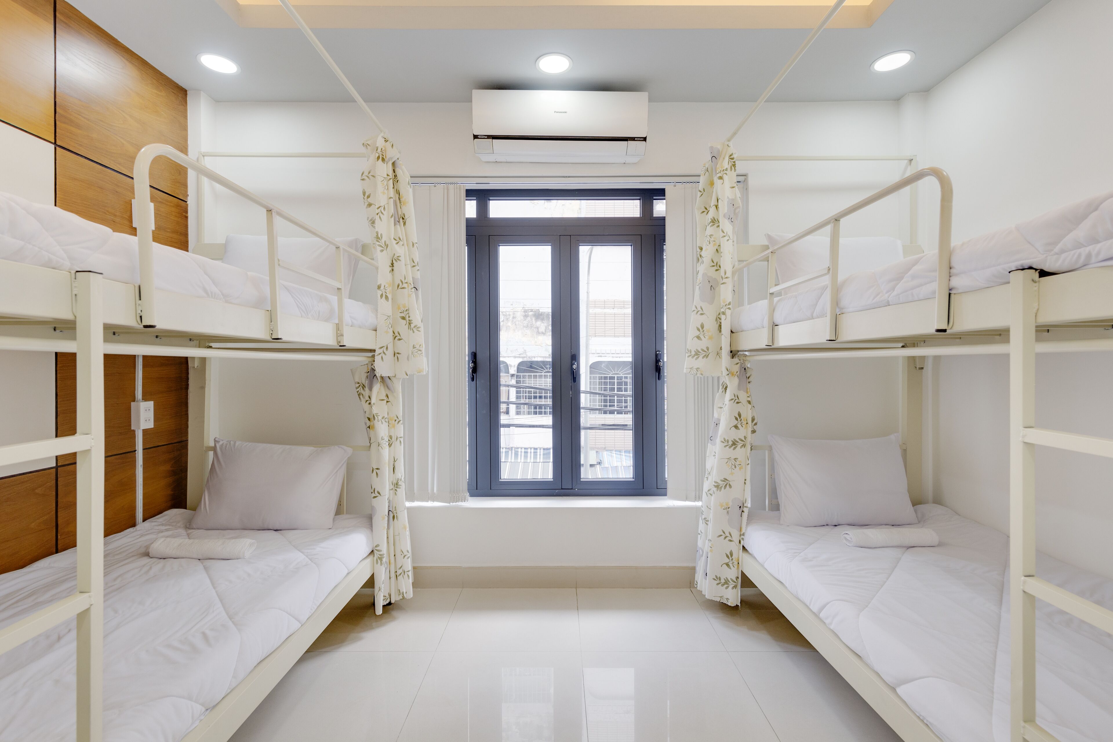 Una habitación limpia y bien iluminada con literas, una ventana con cortinas y un equipo de aire acondicionado.