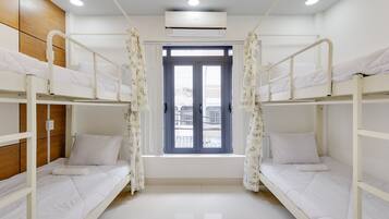 Una habitación limpia y bien iluminada con literas, una ventana con cortinas y un equipo de aire acondicionado.
