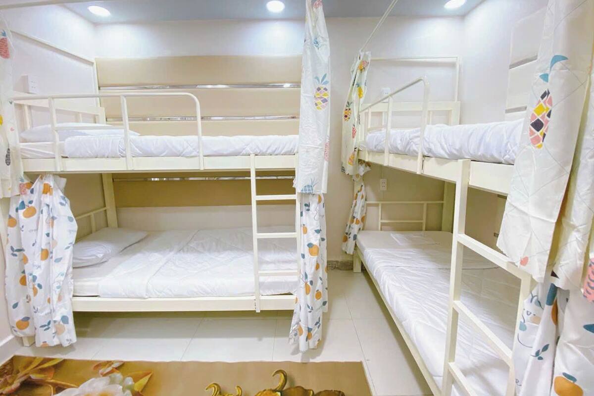 Quarto com beliches, roupa de cama branca e cortinas com motivos de frutas.