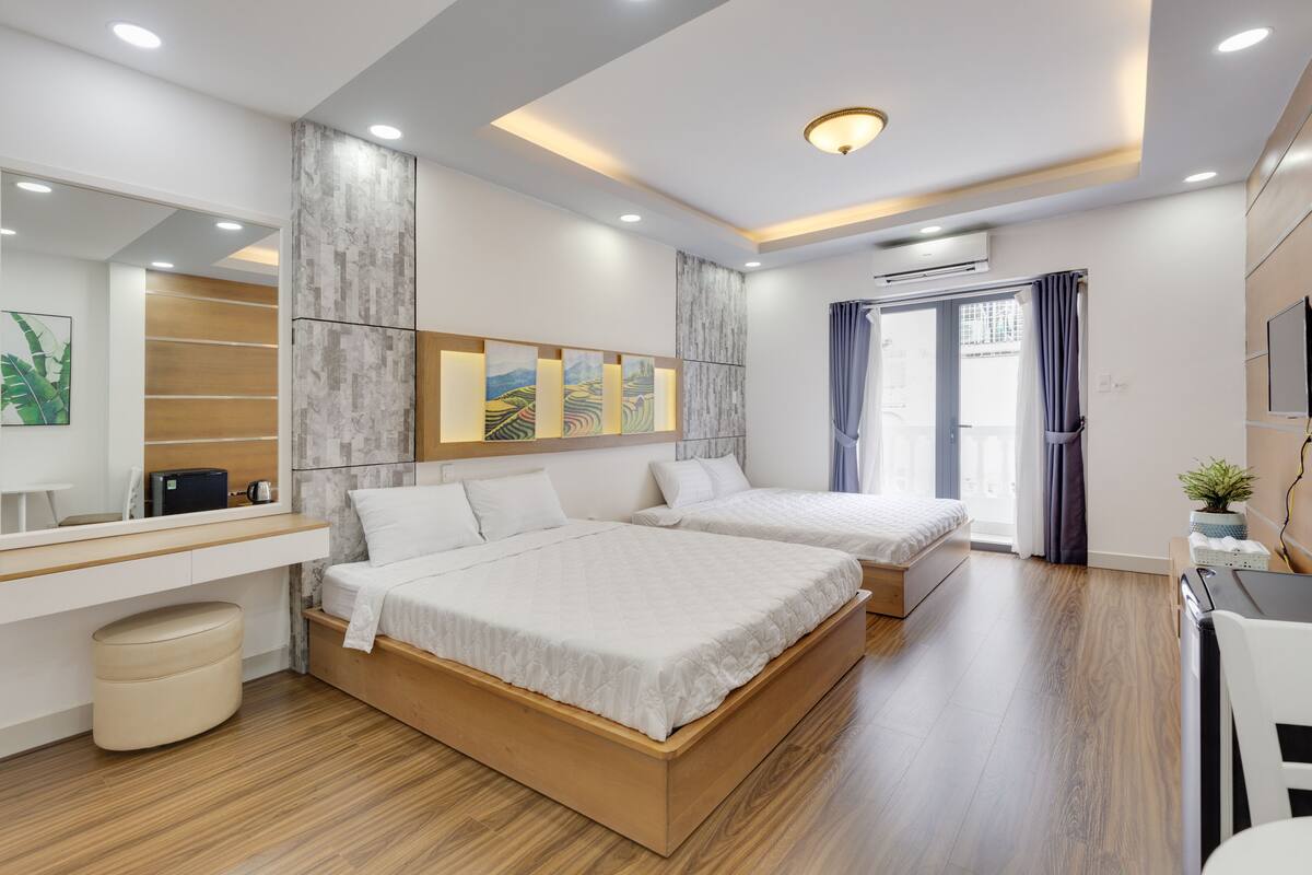 Quarto de hotel moderno com duas camas, uma escrivaninha e uma janela grande com cortinas.