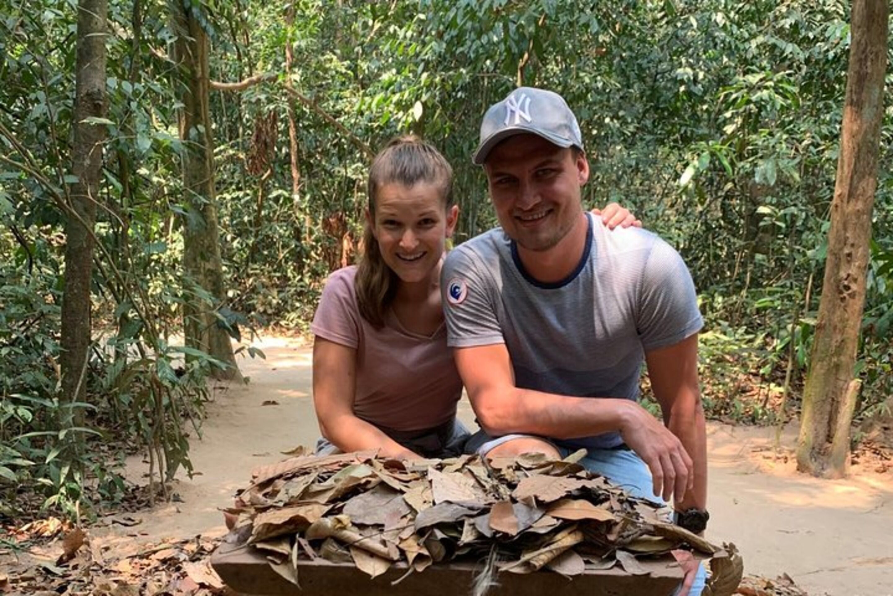 Two people sitting at a table with a pile of leaves in a forested area.