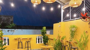 An outdoor seating area with round tables and stools, surrounded by potted plants and hanging wicker lamps. - Saigon Authentic Hostel & Tours (Ho Chi Minh City)