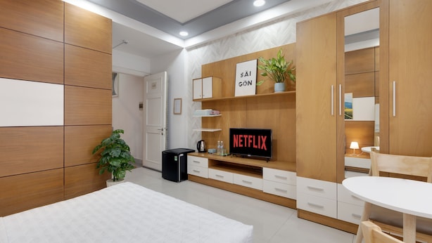 A modern bedroom with a bed, a TV displaying 'NETFLIX', a small desk, and a wardrobe. - Saigon Authentic Hostel & Tours (Ho Chi Minh City)
