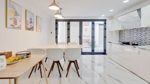 A modern kitchen with white cabinets, a marble floor, and a dining area with a table and chairs. - Saigon Authentic Hostel & Tours (Ho Chi Minh City)