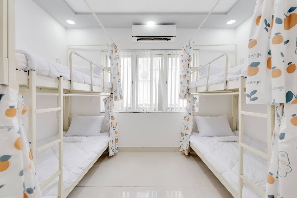 Quarto com beliches, roupa de cama branca, janela com cortinas e aparelho de ar condicionado.