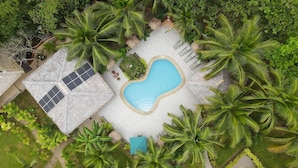 An aerial view of a resort with a swimming pool surrounded by palm trees and a covered area with solar panels. - Denika's Suites (Puerto Princesa)