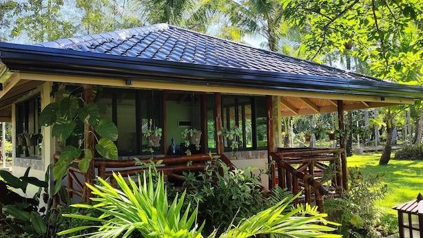 A covered outdoor area with a tiled roof, surrounded by lush greenery and plants. - Denika's Suites (Puerto Princesa)