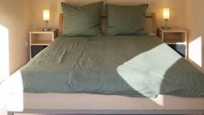 A bedroom with a bed, two bedside lamps, and a painting of red flowers on the wall.