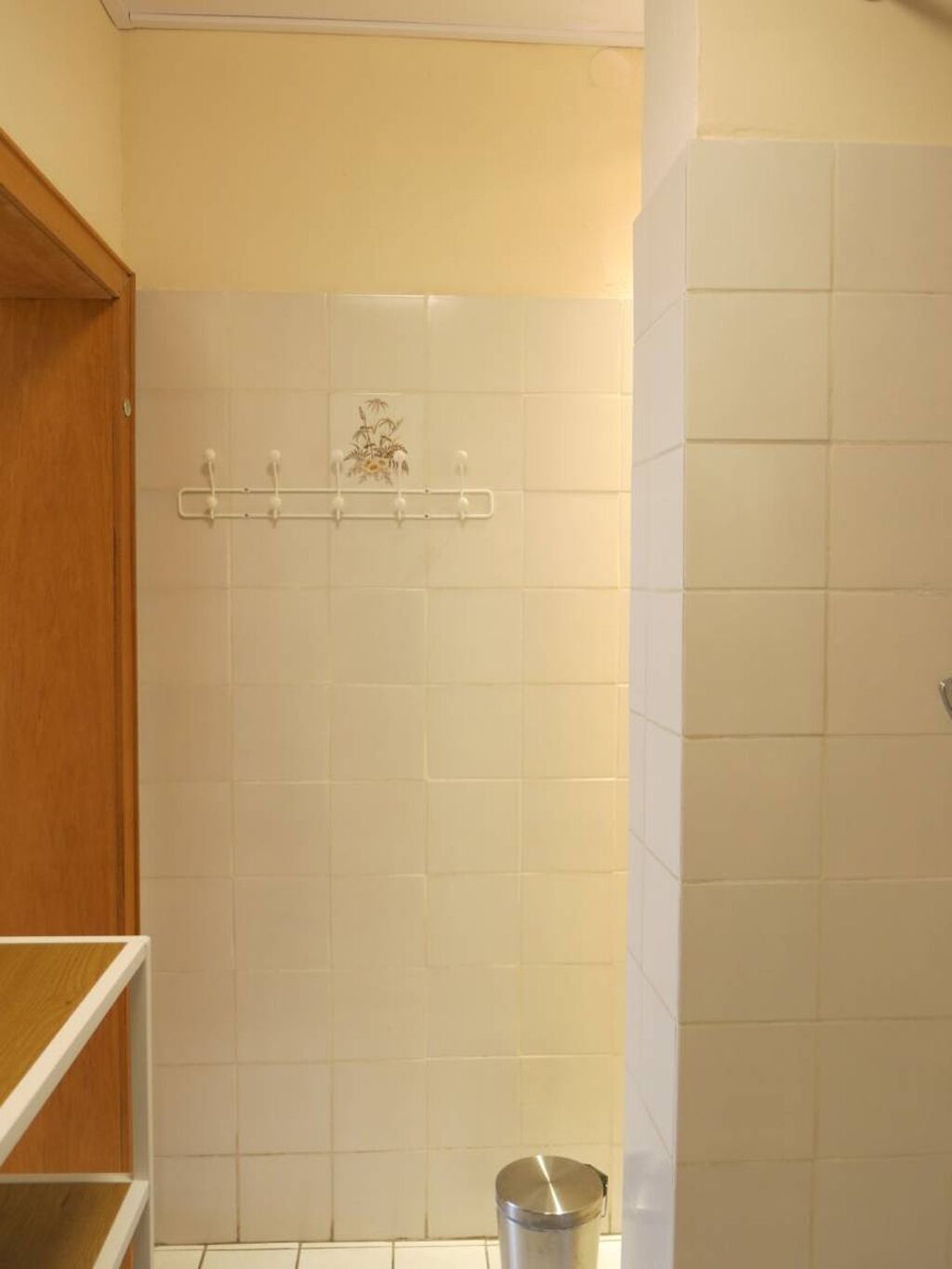 Casa de banho com azulejos brancos, um armário de madeira e um cesto de metal.