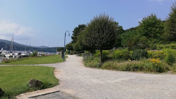 A gravel path leading to a dock with boats, surrounded by greenery and a clear sky.