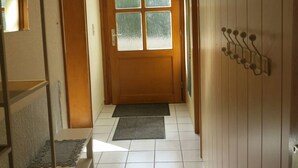 A hallway with a wooden door, a bench, and a wall-mounted rack.