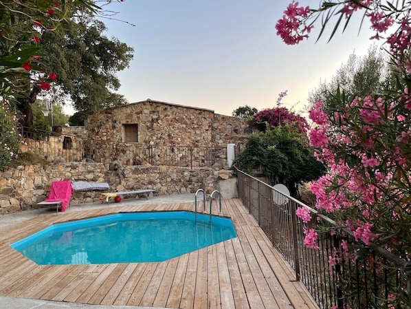 Eine Holzterrasse mit Schwimmbecken, Steinmauern und blühenden, rosa Pflanzen.