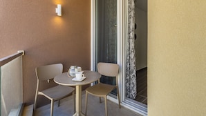 Un petit balcon avec une table ronde et deux chaises, un luminaire blanc fixé au mur et une porte-fenêtre coulissante.