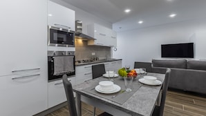 Une cuisine moderne avec des meubles blancs, un four encastré et un coin repas avec une table dressée pour deux personnes.