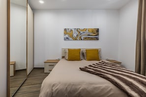 Ein Schlafzimmer mit einem Bett, zwei Nachttischen, einem Spiegel, einem Gemälde und einem Holzboden.