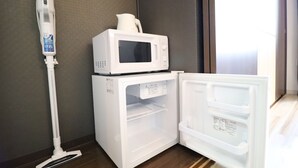 A compact kitchen area with a microwave and a refrigerator, a vacuum cleaner, and a window providing natural light. - Serenite Nippombashi (Osaka)