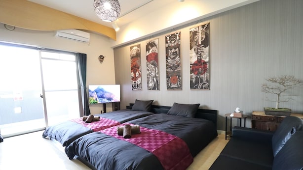A hotel room with a large bed, a sofa, a TV, and artwork on the wall. - Serenite Nippombashi (Osaka)