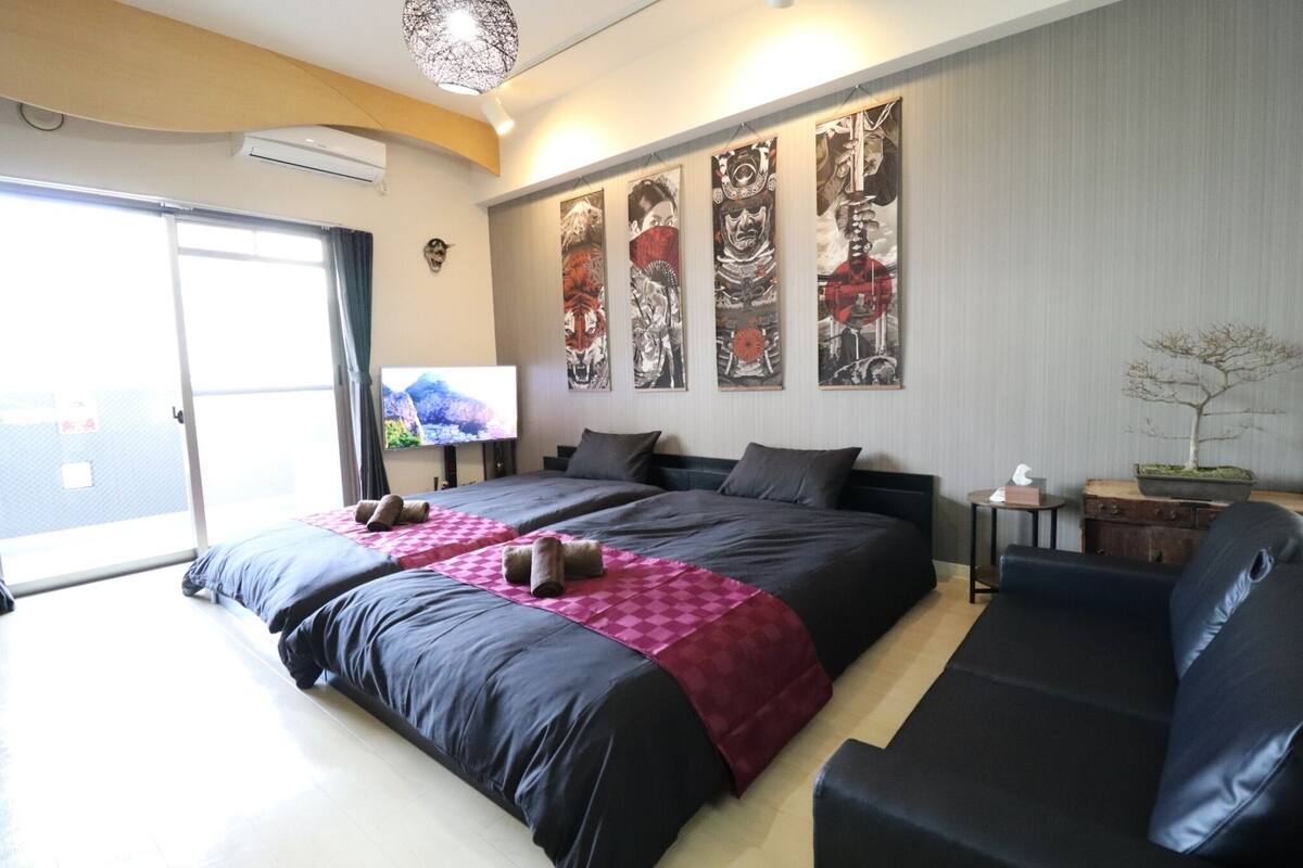 A hotel room with a large bed, a sofa, a TV, and artwork on the wall.