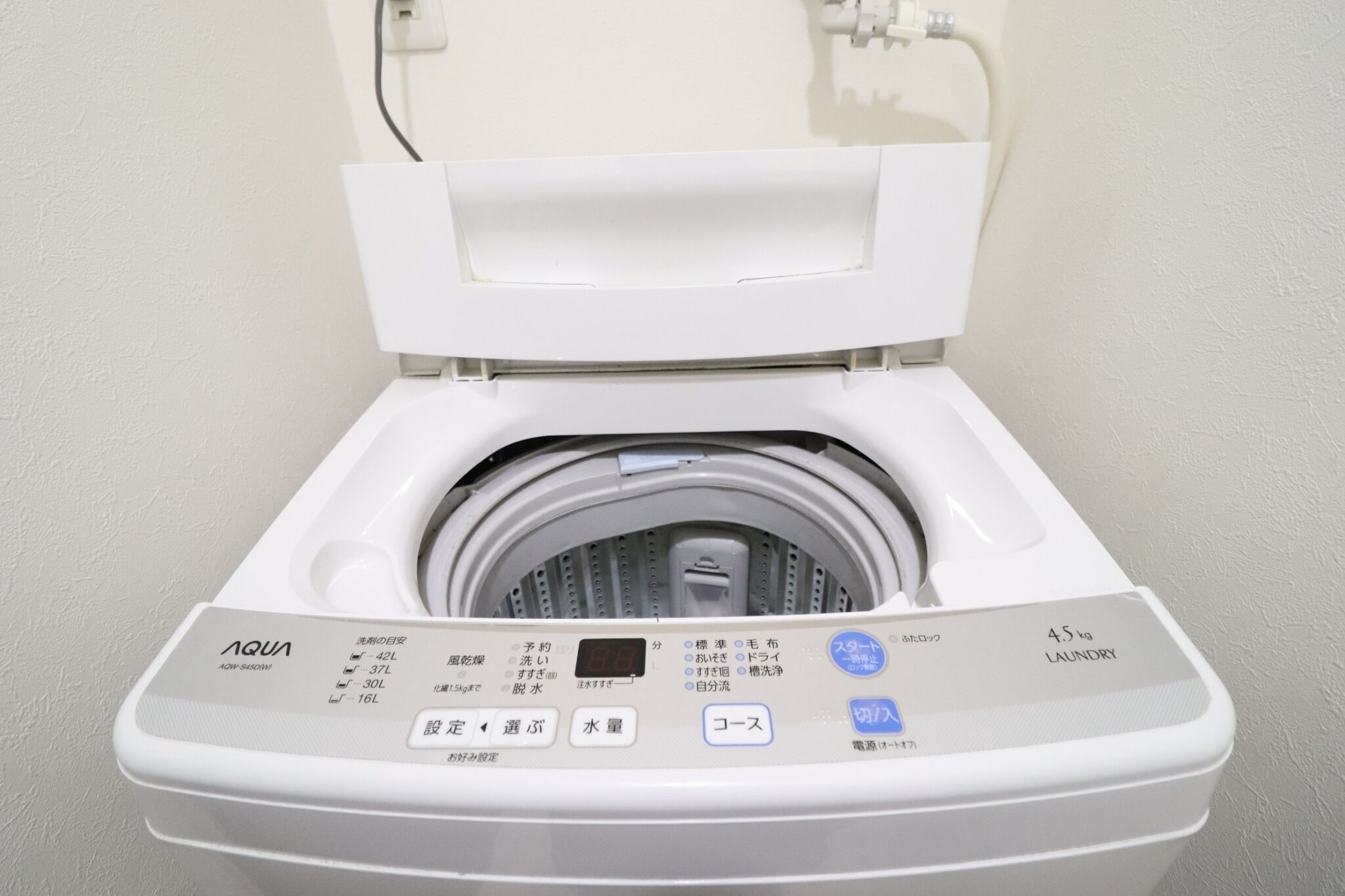 A white, wall-mounted, front-loading washing machine with a digital control panel and a 45 kg capacity label.
