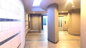 A corridor with tiled walls, a central pillar, and an elevator in the background. - Serenite Nippombashi (Osaka)