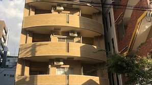 A multi-story building with a curved facade, air conditioning units on each floor, and a ground-level entrance with a motorcycle parked outside. - Serenite Nippombashi (Osaka)