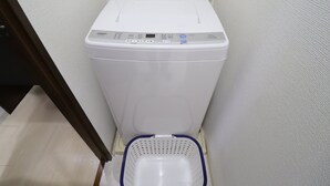 A white washing machine with a control panel, a blue laundry basket, and a tiled floor. - Serenite Nippombashi (Osaka)