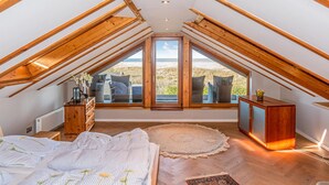 A bedroom with a sloped ceiling, large windows, a bed with floral bedding, a wooden dresser, and a rug. - Cozy home in Lübeck with house sea view (Lübeck)