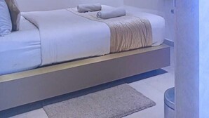 Een moderne slaapkamer met een bed, kussens, een nachtkastje, een televisie en een wandlamp.