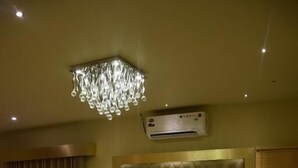 Een hotelkamer met een groot bed, een gestapeld hoofdeinde, een kroonluchter, een airconditioningapparaat en een nachtkastje met een fles.