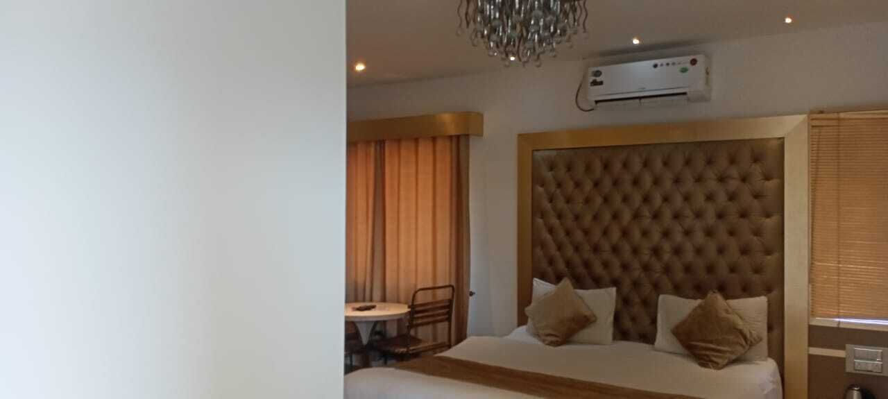 Et hotelværelse med en betrukken sengegavl, en seng med to puder, et lille bord med en stol og en aircondition-enhed på væggen.